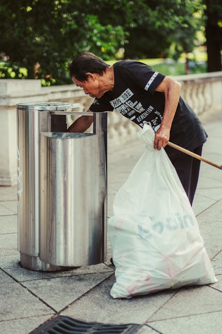 An overview of a large ongoing rubbish clearance operation in an outdoor, gravel-covered area showing three individuals sorting through a diverse collection of waste materials. One person in a red and